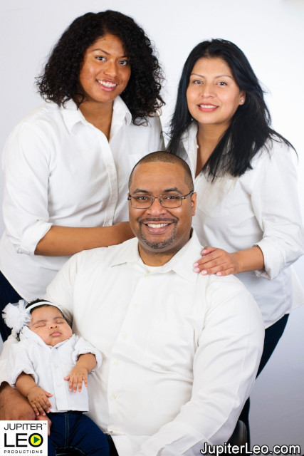 Family portrait of father, mother, teenage daughter and newborn daughter against white background.