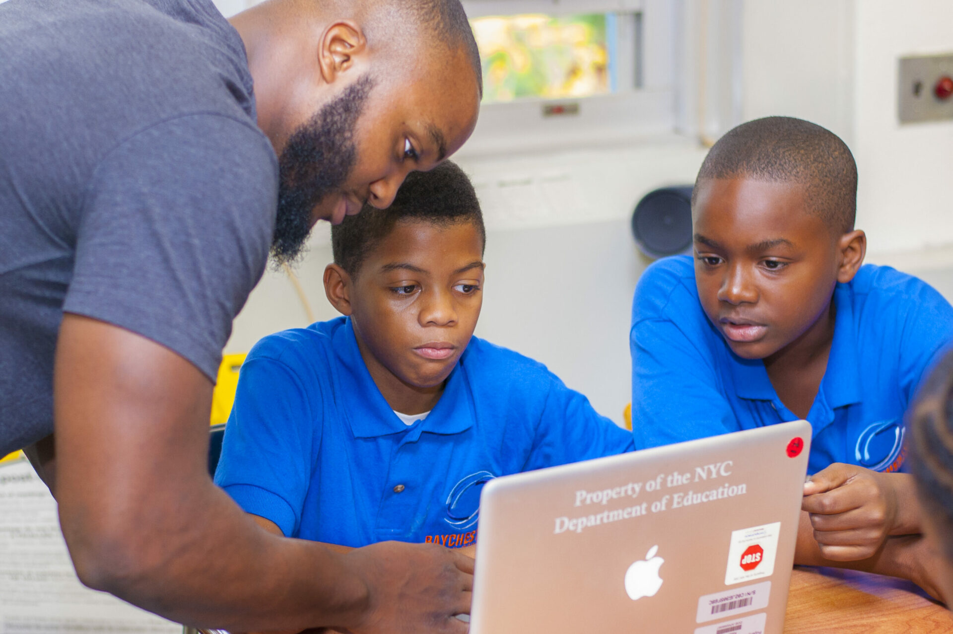 African american teacher helping two students on a computer.