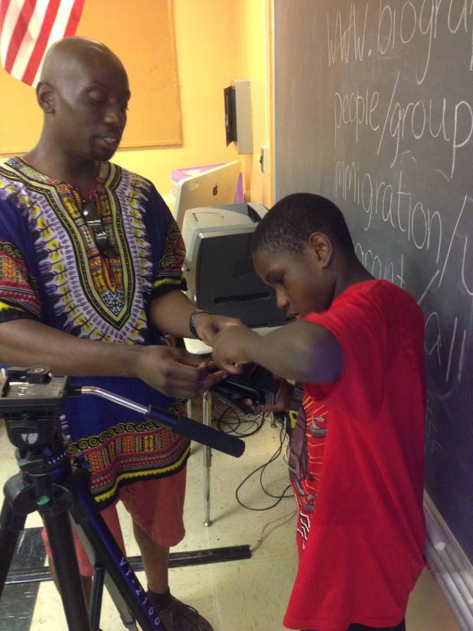 A student receives help putting on a tripod plate on a camera.
